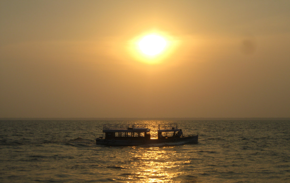 Photograph of an old boat in the sea with the sun setting in the background. Tittle: Sailing by Sreelekha Chatterjee